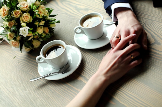 Фото Свадебная пара держится за руки с чашками кофе за деревянным столом