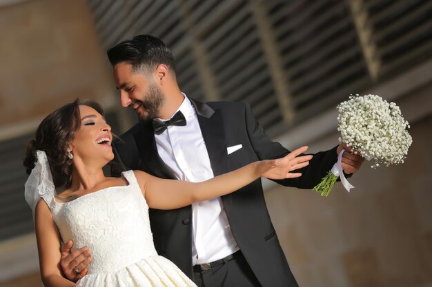 金色の石の背景に花束を持つ結婚式のカップルの夫と妻