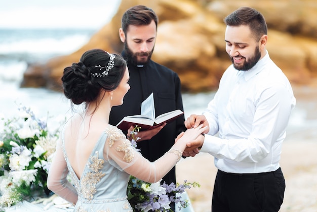Foto sposi vicino all'oceano con un prete