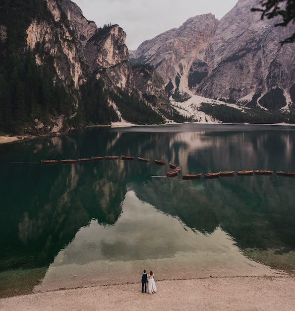 The wedding couple stands on shore lake high stone mountains