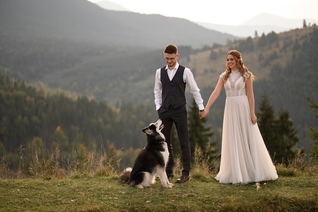 Wedding couple with dog in mountains at sunset romantic evening in mountains