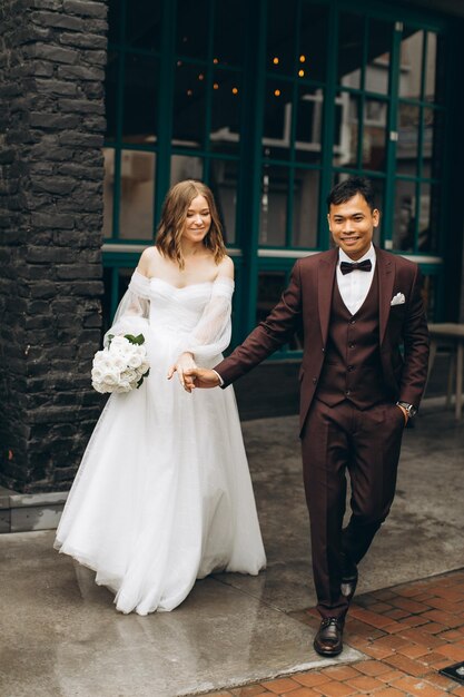 Wedding day Beautiful European bride and her Asian groom posing against the backdrop of cafes and large windows