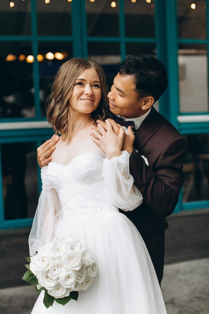 Wedding day Beautiful European bride and her Asian groom posing against the backdrop of cafes and large windows