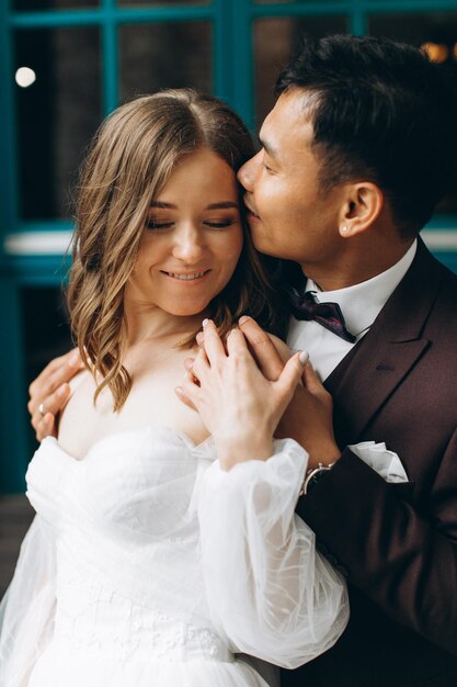 Wedding day Beautiful European bride and her Asian groom posing against the backdrop of cafes and large windows