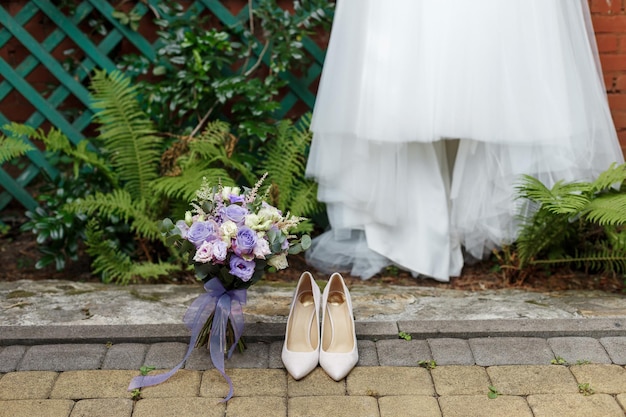 Wedding details classic bride shoes and bouquet of roses standing on the background pf dress and