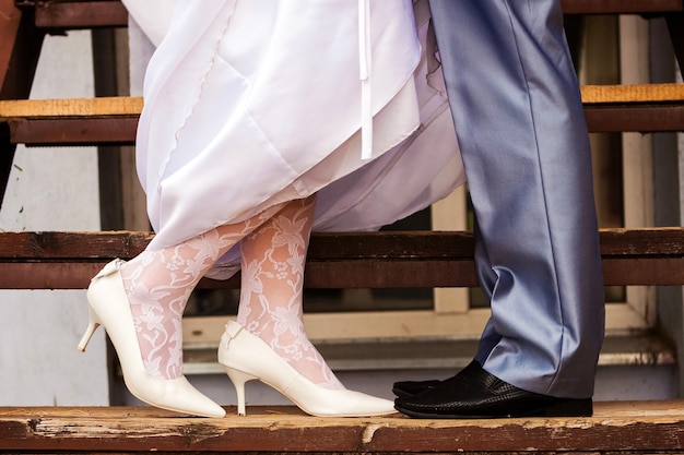 Dettagli del matrimonio: gambe della sposa in collant di pizzo e sposo sui gradini di legno delle scale