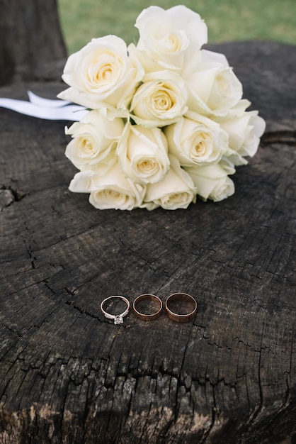 Wedding details wedding gold rings with diamond and wedding\
bouquet of white roses on the wooden background