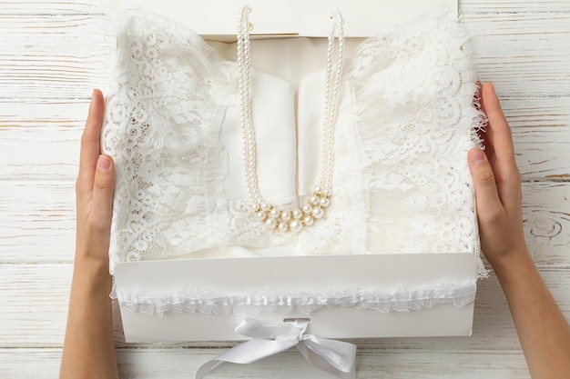 Wedding dress and beads in box in female hands on wooden background top view