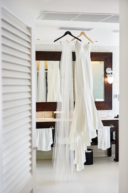 Wedding dress and long veil hanging in the white room