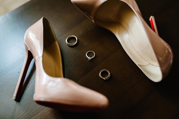 Фото Свадебные золотые кольца и стильные элегантные классические лакированные бежевые туфли на деревянном фоне крупным планом вид сверху