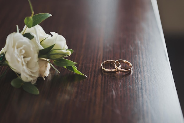 Wedding gold rings lie with white flowers on a brown table 2595