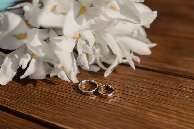 Wedding gold rings lie on a wooden table with a bride39s bouquet