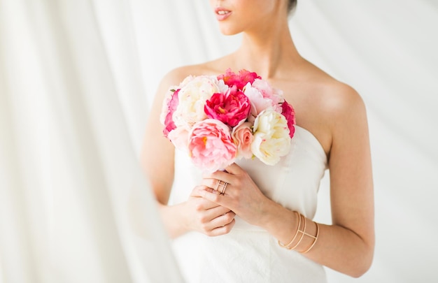 wedding, holidays, beauty, jewelry and luxury concept - close up of beautiful woman or bride with flower bouquet wearing golden ring and bracelet