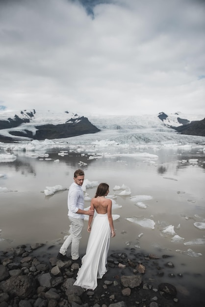 アイスランドでの結婚式。青い氷の上に立っている間、白いドレスを着た男と女が抱き合っています