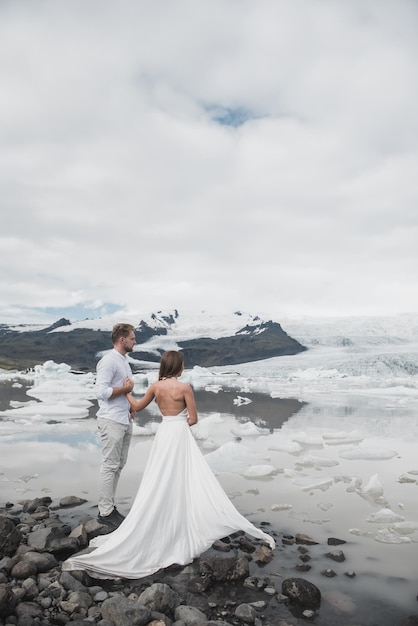 アイスランドでの結婚式。青い氷の上に立っている間、白いドレスを着た男と女が抱き合っています