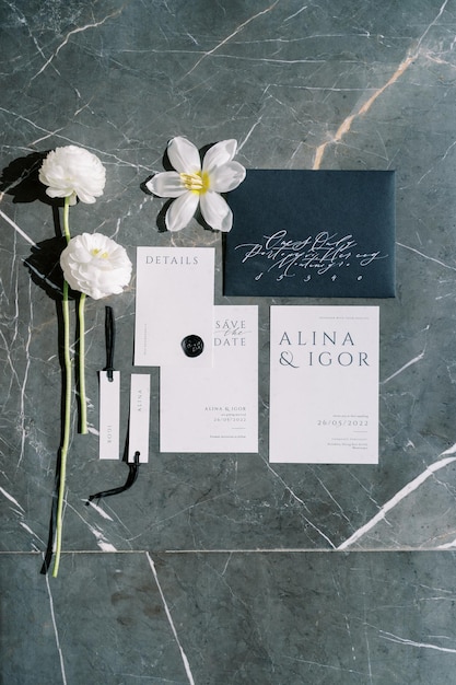 Photo wedding invitations name cards and white flowers lie on a black marble table