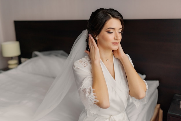 Wedding morning preparation. Bride portrait at wedding morning. Bride touches her hairstyle and rejoices.