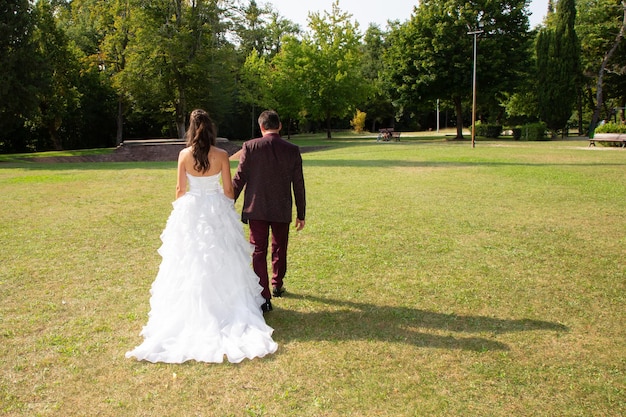 Wedding newlyweds couple in green park in behind rear view walking in love