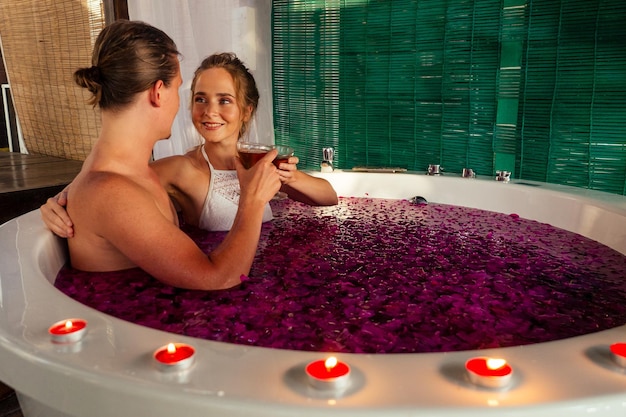 Notte di nozze.bella sposa e sposo bello che si rilassano nella vasca da bagno fiori tropicali presso l'hotel di lusso resort.coppia innamorata di bicchieri tintinnanti eco bali spa.candele,data romantica san valentino 14 febbraio,