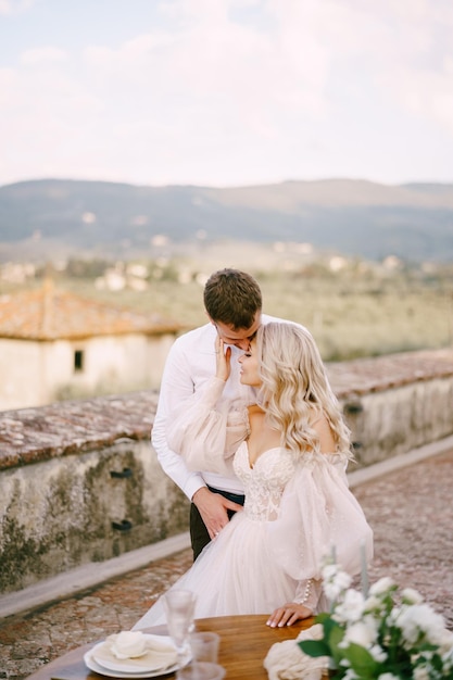 이탈리아 투스카니의 오래된 와이너리 빌라에서의 결혼식 신랑은 지붕에서 신부를 껴안고 키스합니다.