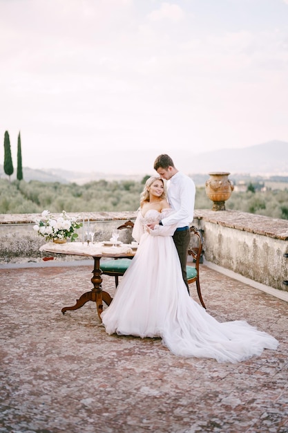 イタリア、トスカーナの古いワイナリーヴィラでの結婚式結婚式のカップルがテーブルの近くに立って