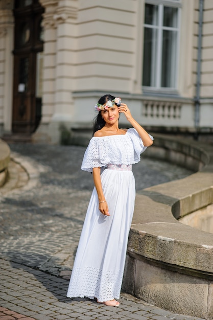 Wedding photo shoot. Portrait of a charming bride in a wreath on her head. The woman is smiling. Shot on the background of an old building. Rustic or boho style wedding photo.