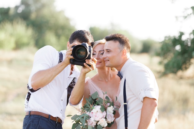 Photo wedding photographer takes pictures of bride and groom in nature. photographer shows just taken photos to wedding couple