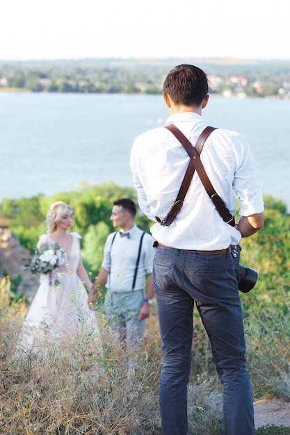 Il fotografo di matrimoni scatta foto della sposa e dello sposo nella natura. sposi sul servizio fotografico. fotografo in azione