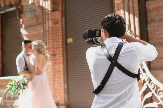 Фото Свадебный фотограф фотографирует жениха и невесту в городе. свадебная пара на фотосессии. фотограф в действии