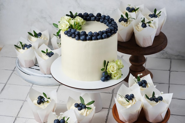 Wedding preparations White wedding cake and cupcakes in the same style decorated with fresh blueberries and flowers