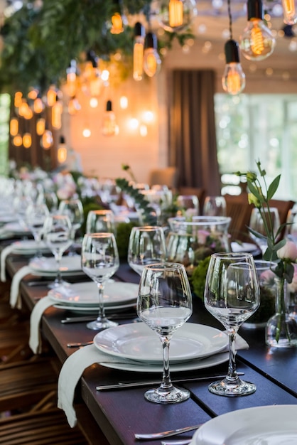 Tavolo per ricevimento di nozze con lampadine edison e decori di verde.