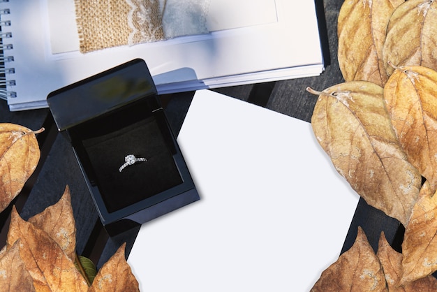 Photo wedding ring in black box on white blank paper with dry leafs decoration