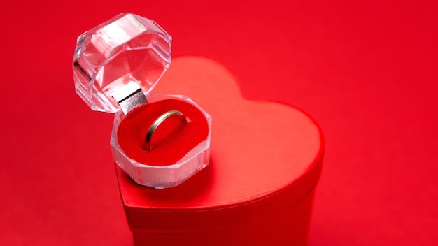 Обручальное кольцо и коробка в форме сердца на красном фоне