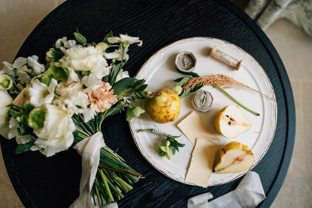 Photo wedding ring lies in a box on a white plate next to pears and green twigs a plate with a bouquet of