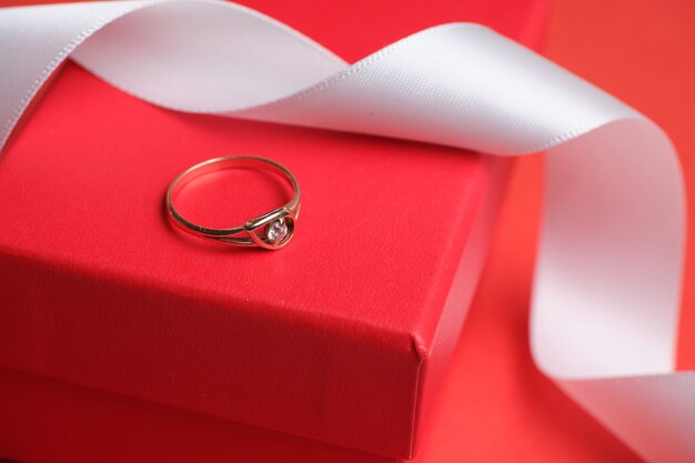 Wedding ring on a red gift box and a white ribbon.