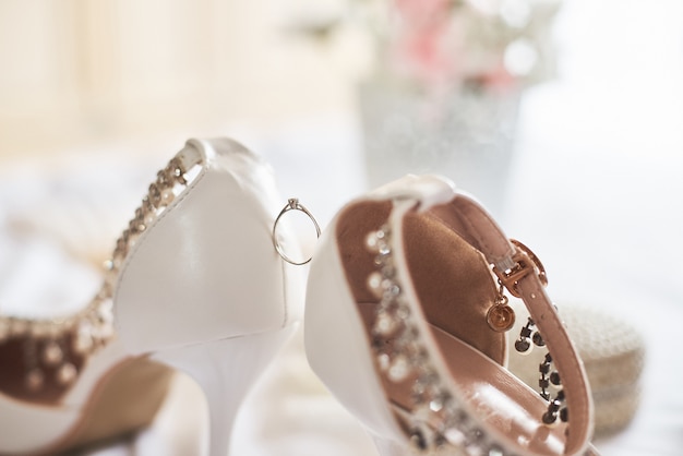 Wedding ring between white bridal shoes.