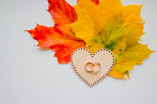 Wedding ring on wooden heart on autumn leaves background. golden wedding rings