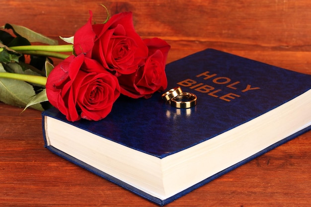 Wedding rings on bible with roses on wooden background