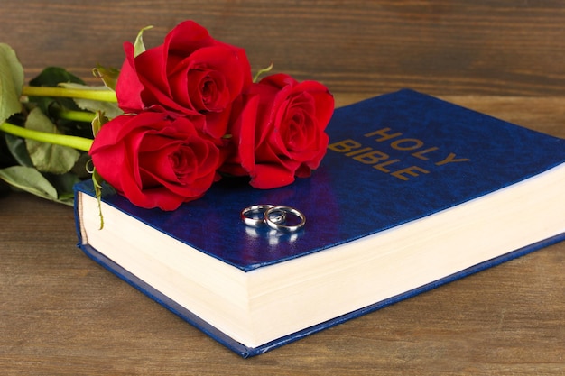 Wedding rings on bible with roses on wooden background