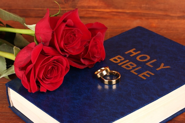 Wedding rings on bible with roses on wooden background