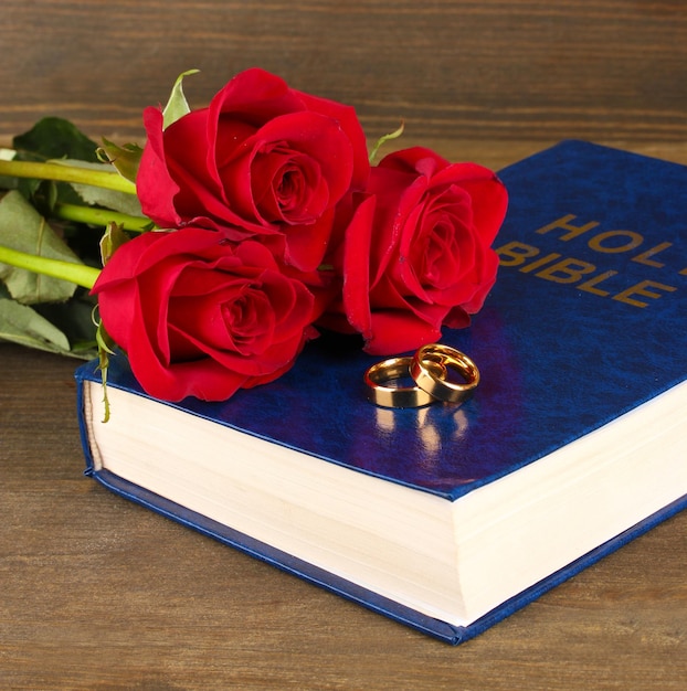 Wedding rings on bible with roses on wooden background