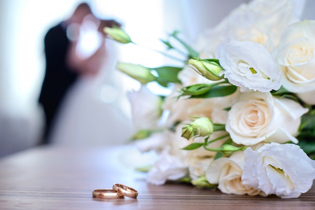 Wedding rings and bouquet on a of blurred newlyweds