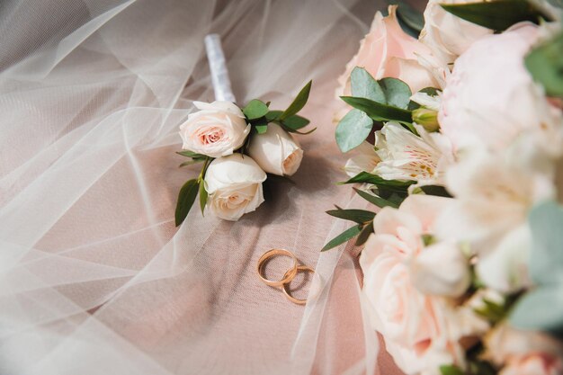 Wedding rings and boutonniere lie on the veil next to the bride's bouquet