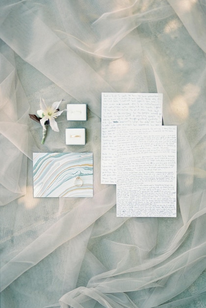 Photo wedding rings in boxes lie on the veil near the boutonniere and vows of the bride and groom