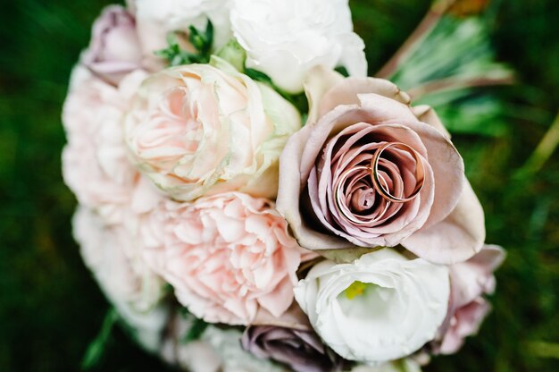 Обручальные кольца невесты и жениха, букет невесты с нежными пастельными цветами и розовыми розами и зеленью, лежащими на траве. Осень. плоская планировка. вид сверху.