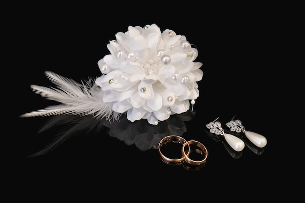 Wedding rings earrings of the bride and groom's boutonniere on black background Wedding symbols