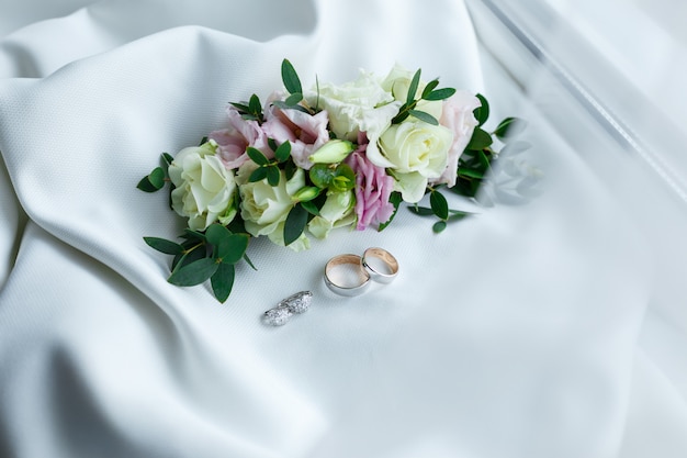 Wedding rings and earrings lying near gentle hairpin with flowers