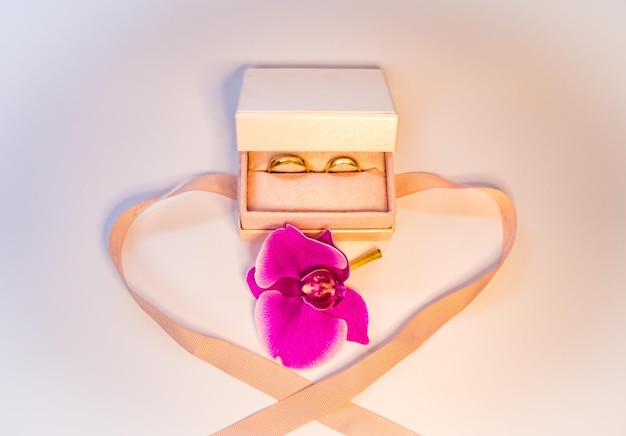 Свадебные кольца в подарочной коробке с фиолетовыми орхидейными золотыми украшениями свадьбы
