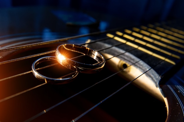 Обручальные кольца на крупном плане струн гитары на темном фоне.