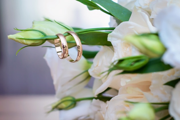 Обручальные кольца висят на веточке свадебного букета